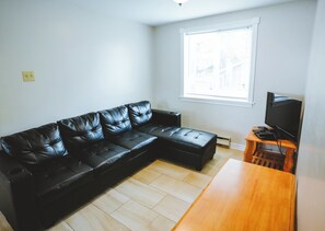 A living room with a black leather sectional sofa, a wooden coffee table, and a television on a wooden stand. - Cardinal Cottage - 3 Bedrooms (Trent Lakes)