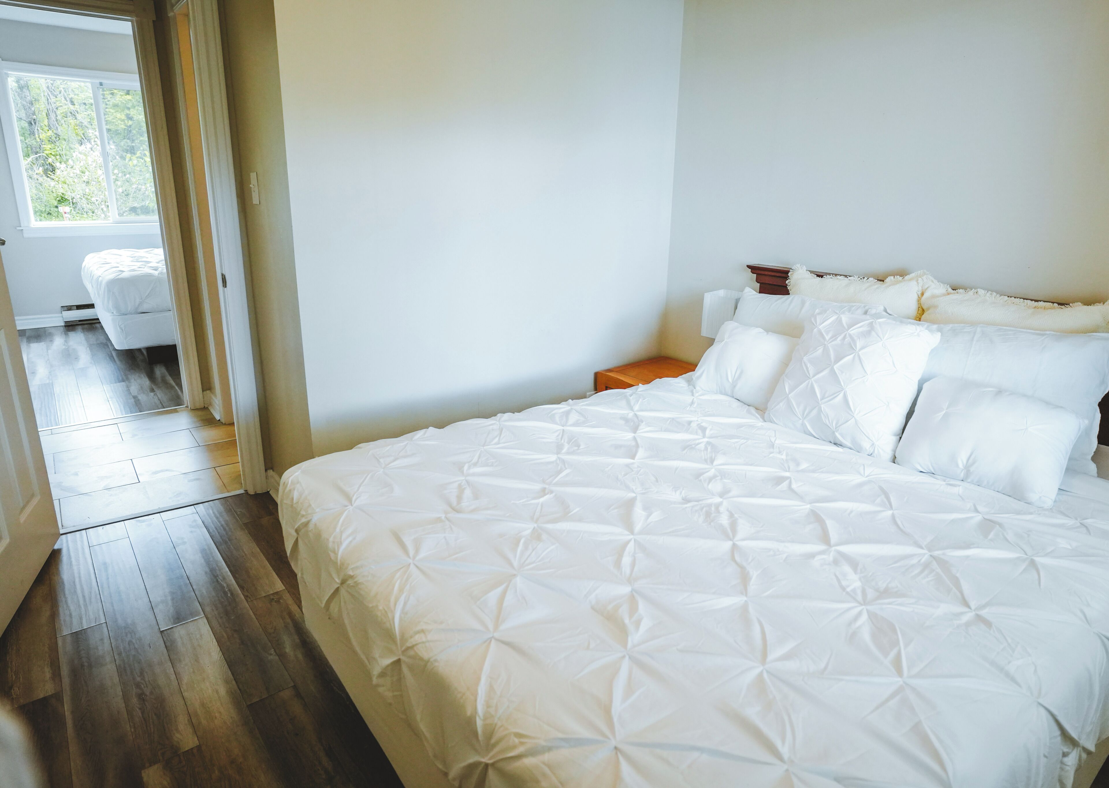 Une chambre avec un grand lit, une table de chevet en bois et une fenêtre donnant sur un paysage verdoyant.