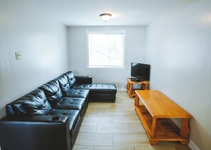 A living room with a black leather sofa, a wooden coffee table, and a television on a wooden stand. - Cardinal Cottage - 3 Bedrooms (Trent Lakes)