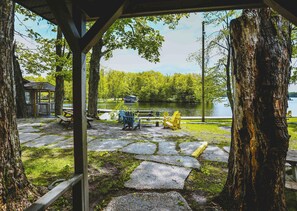 A lakeside pavilion with stone steps leading to a dock, surrounded by trees and a view of the lake. - Cardinal Cottage - 3 Bedrooms (Trent Lakes)