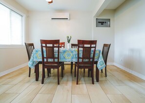 A dining area with a table set for four, surrounded by chairs, a window with blinds, an air conditioning unit, and a wall-mounted electrical panel. - Cardinal Cottage - 3 Bedrooms (Trent Lakes)