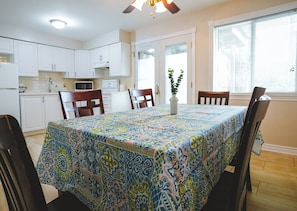 A dining area with a patterned tablecloth, white cabinets, and a ceiling fan. - Cardinal Cottage - 3 Bedrooms (Trent Lakes)