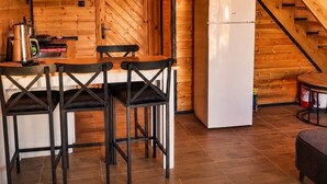 Interior de madera con área de cocina, una mesa de comedor con sillas y una escalera que sube a un nivel superior.