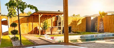 Un jacuzzi bajo una pérgola de madera con patio trasero, zona de barbacoa y piscina.