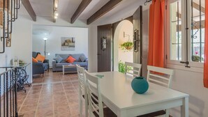 A dining area with a white table and chairs, a blue vase, and a view of the living room through an open door. - Pollensa Mountain View Villa (Pollença)