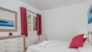 A bedroom with a bed, a chair, a dresser, and a window with curtains. - Pollensa Mountain View Villa (Pollença)
