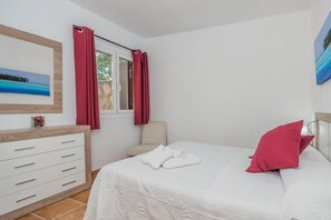 Ein Schlafzimmer mit einem Bett, einem Sessel, einer Kommode und einem Fenster mit Vorhängen.