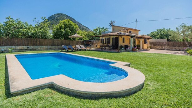A backyard with a swimming pool, a wooden deck, and a house with a mountain in the background. - Pollensa Mountain View Villa (Pollença)