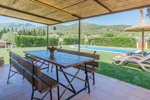 Eine Terrasse im Freien mit Holztisch und -bänken, einem Pool und Blick auf eine gebirgige Landschaft.