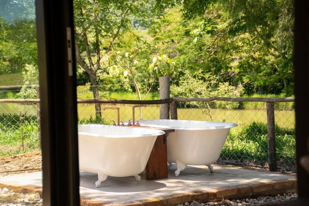 Due vasche da bagno in stile vintage su una piattaforma in cemento, circondate da una recinzione in legno e vegetazione.
