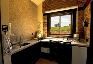 A compact kitchen with a window, a sink, a stove, and a refrigerator. - Chalés Ipês da Serra (Serra Negra)