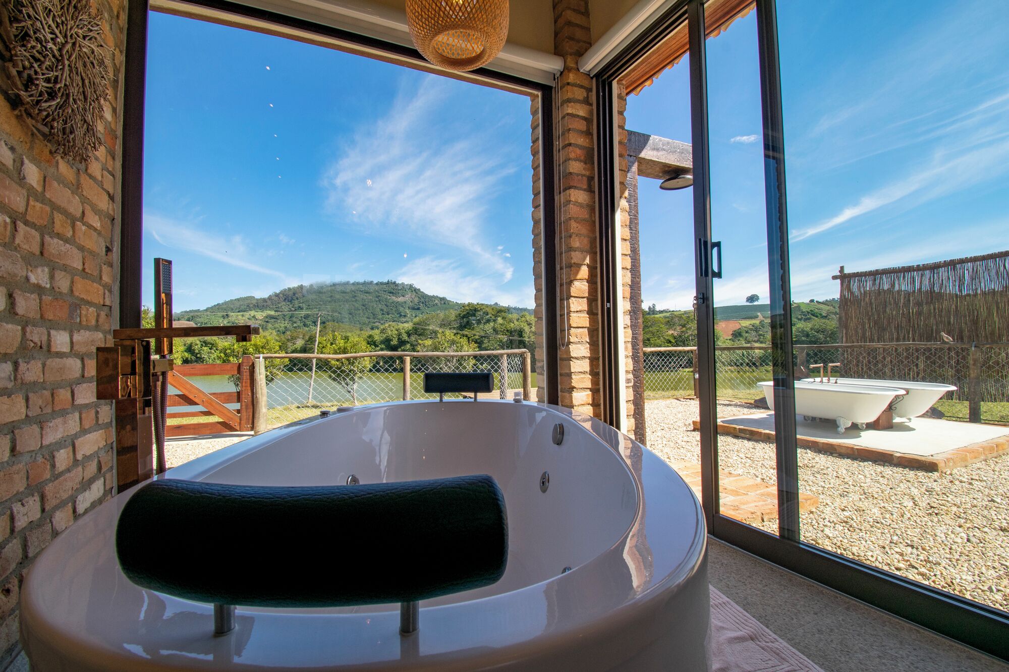 A spa area with a large bathtub, a wooden bench, and a view of a hilly landscape through large windows.