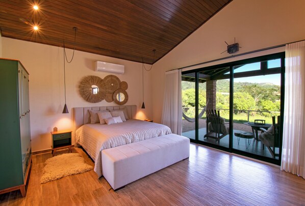 A bedroom with a large bed, a view of the outdoors through a sliding glass door, and a wooden ceiling.