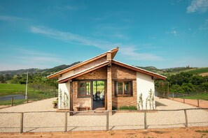 Une maison de plain-pied avec un toit en pente, une cour clôturée et une vue sur des collines verdoyantes en arrière-plan.