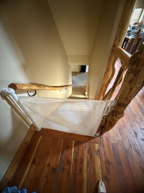 Een hangmat bevestigd tussen houten balken in een kamer met houten vloer en een zichtbare trap.