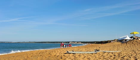 Una playa arenosa con cielo despejado, algunas personas y una tabla de surf en la arena.