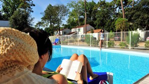 A poolside area with a person reading a book, a pool, and a white fence.