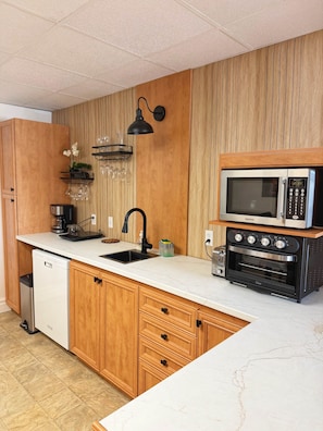 A modern kitchen with wooden cabinets, a white countertop, a built-in microwave, and a dishwasher. - Rez de Jardin at Magog: Waterfront•Pool•Hot tub•3 rooms (Magog)