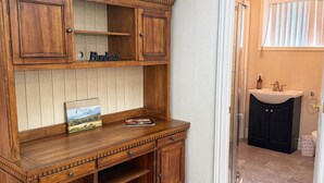 Et træskab med flere skuffer og hylder, en bog med titlen 'Cantina del Post', og en lille flaske på bordpladen.