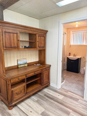 A wooden cabinet with multiple drawers and shelves, a book titled 'Cantina del Post,' and a small bottle on the countertop. - Bord de l’eau Magog : Le Rez-de-Jardin (Magog)