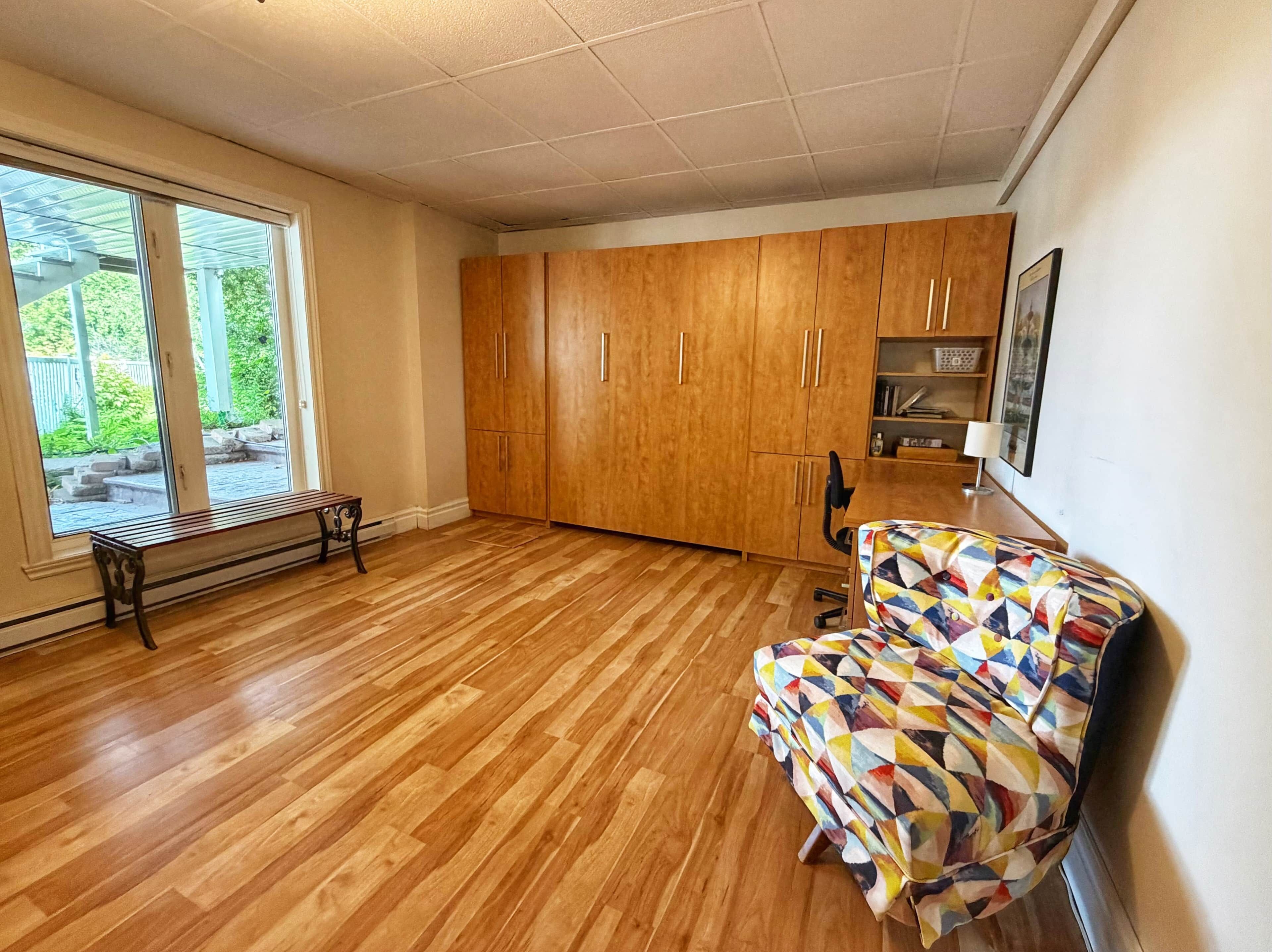 Quarto com piso de madeira, um banco, uma cadeira colorida e um armário de madeira.
