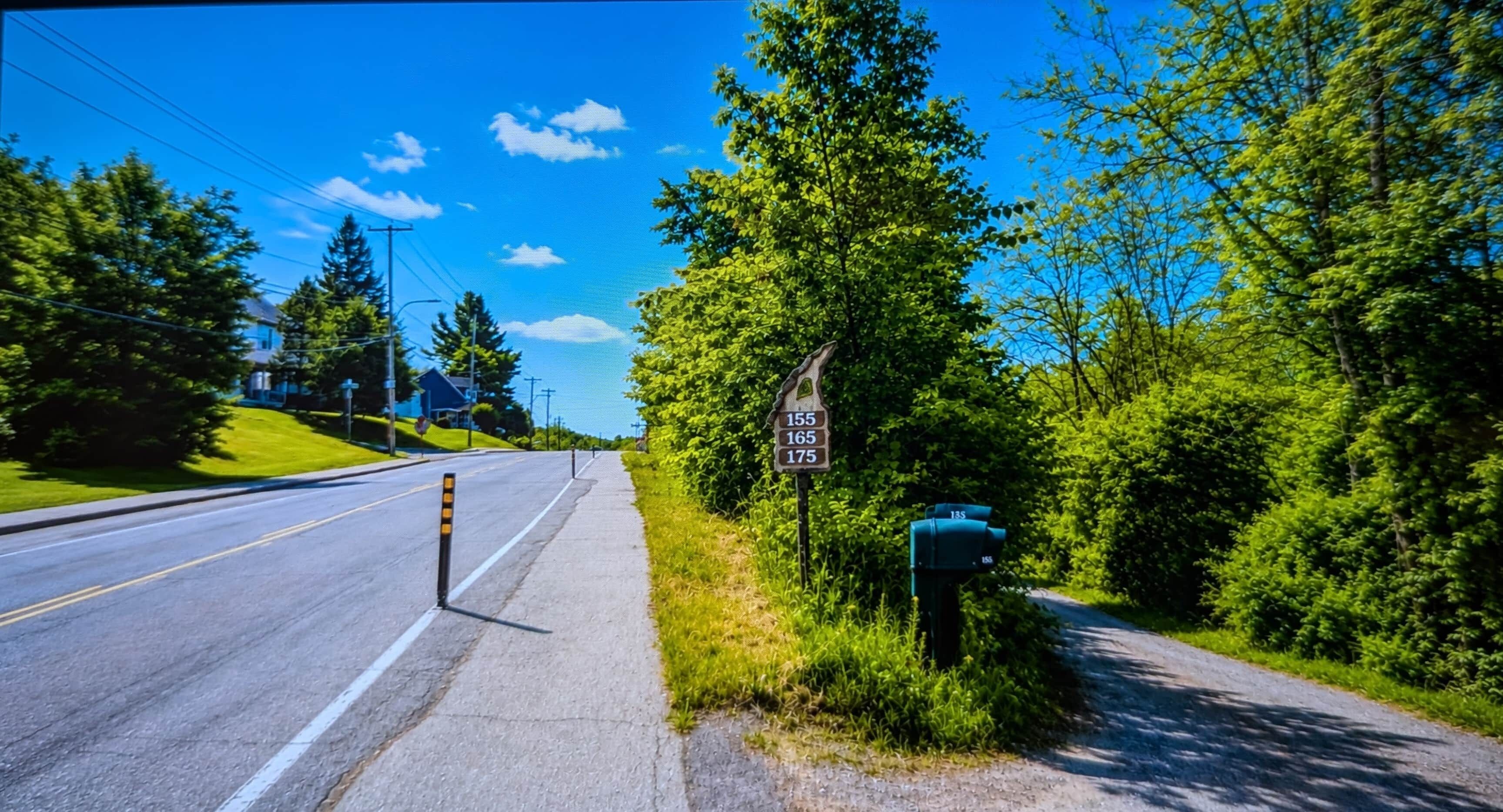 A road with a sidewalk, a mailbox, and a signpost with numbers.