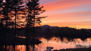 Fredfyldt søudsigt med solnedgang, træer og en moler.
