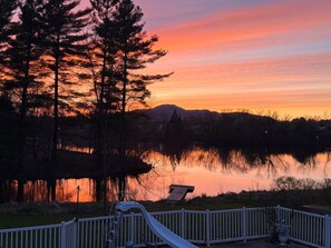 A serene lakeside view with a sunset, trees, and a dock. - Bord de l’eau Magog : Le Rez-de-Jardin (Magog)