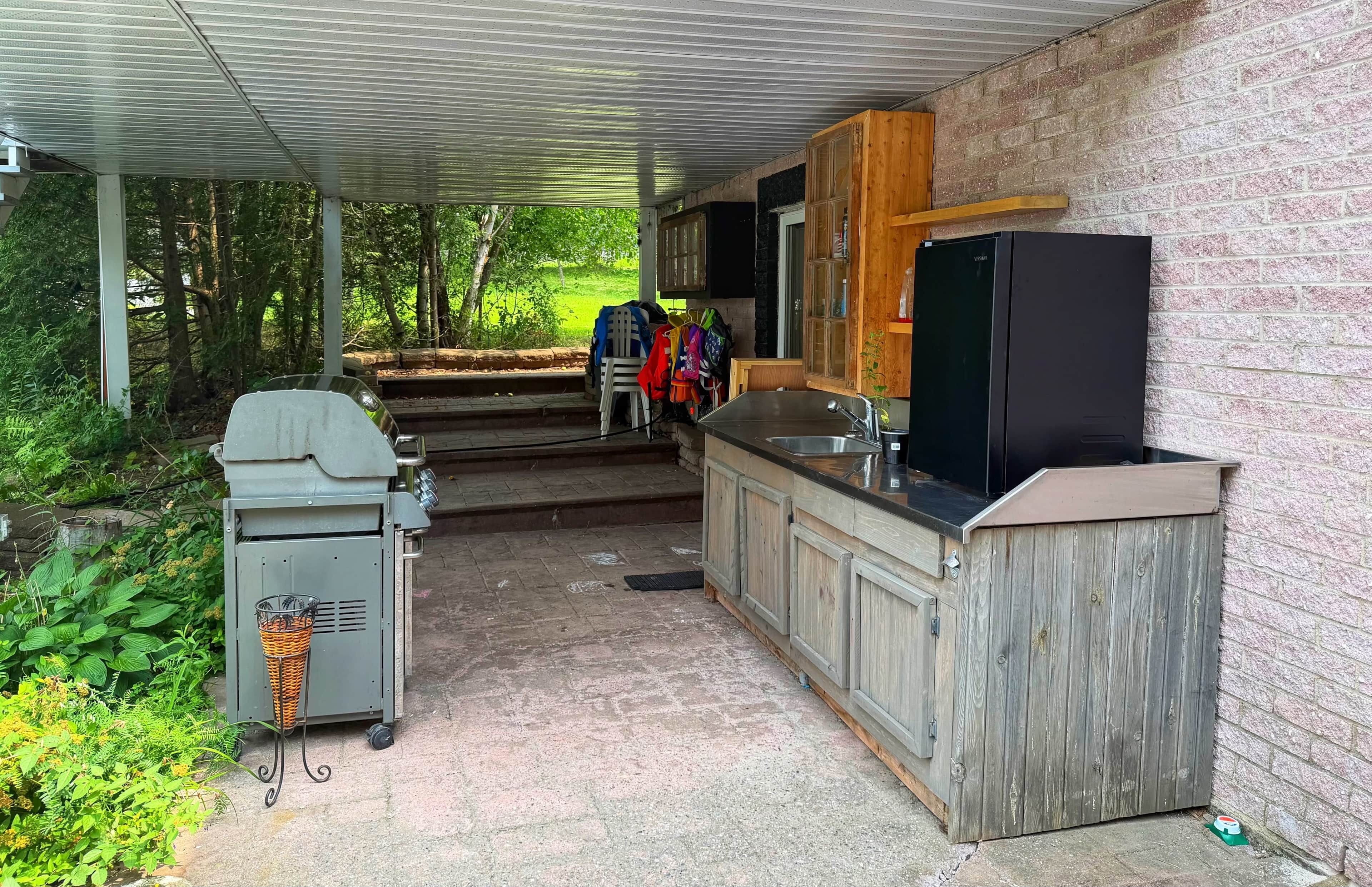 An outdoor kitchen area with a grill, a sink, and wooden cabinets.