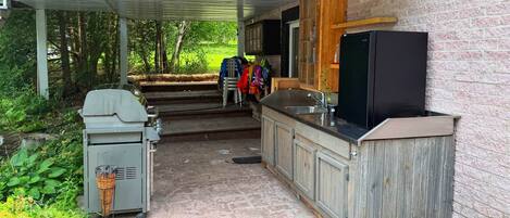 An outdoor kitchen area with a grill, a sink, and wooden cabinets.