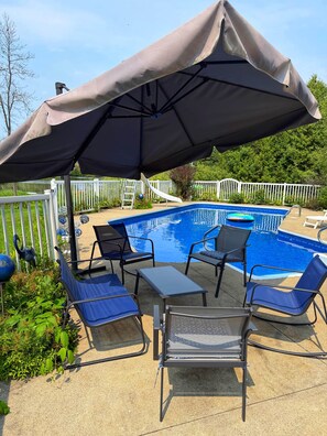 A poolside area with a pool, lounge chairs, and a covered umbrella. - Bord de l’eau Magog : Le Rez-de-Jardin (Magog)