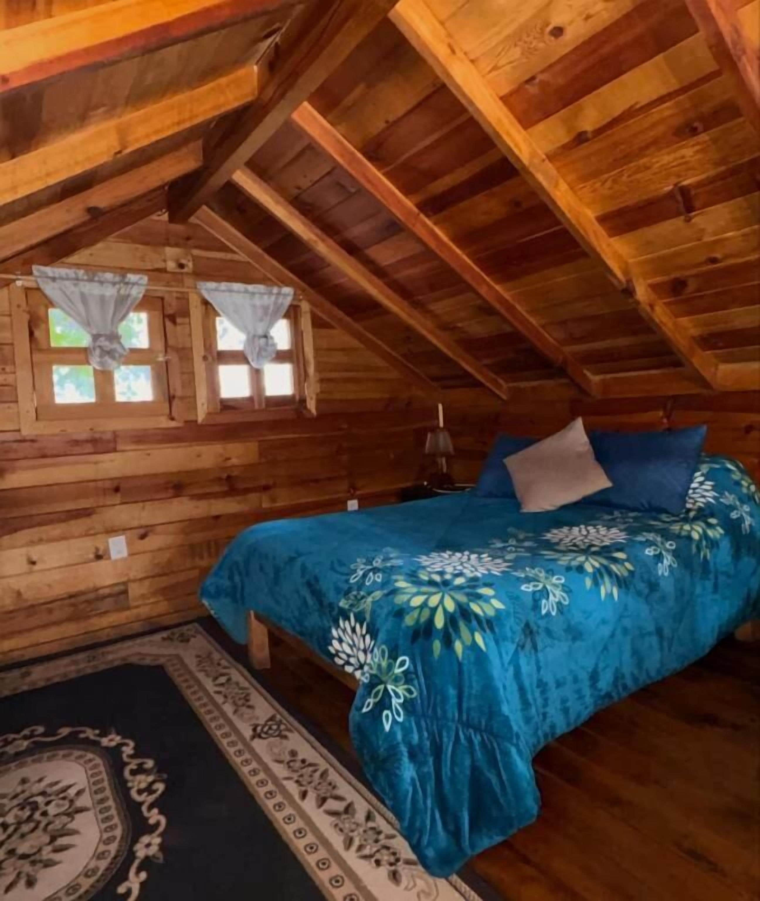 A wooden cabin room with a bed, a window, and a rug.