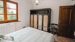 Et soveværelse med seng, radiator, garderobeskab, stol og vindue.