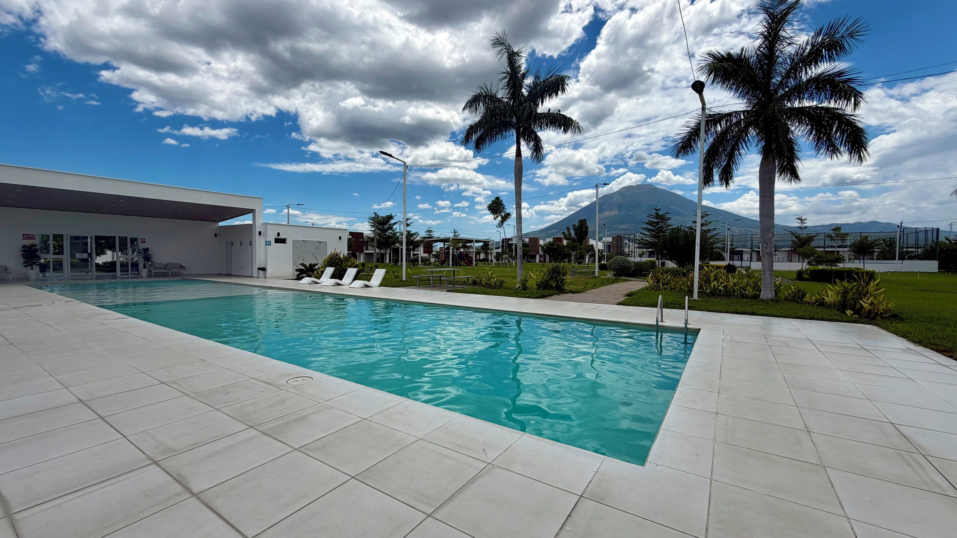 A swimming pool with lounge chairs, a modern building, and palm trees.