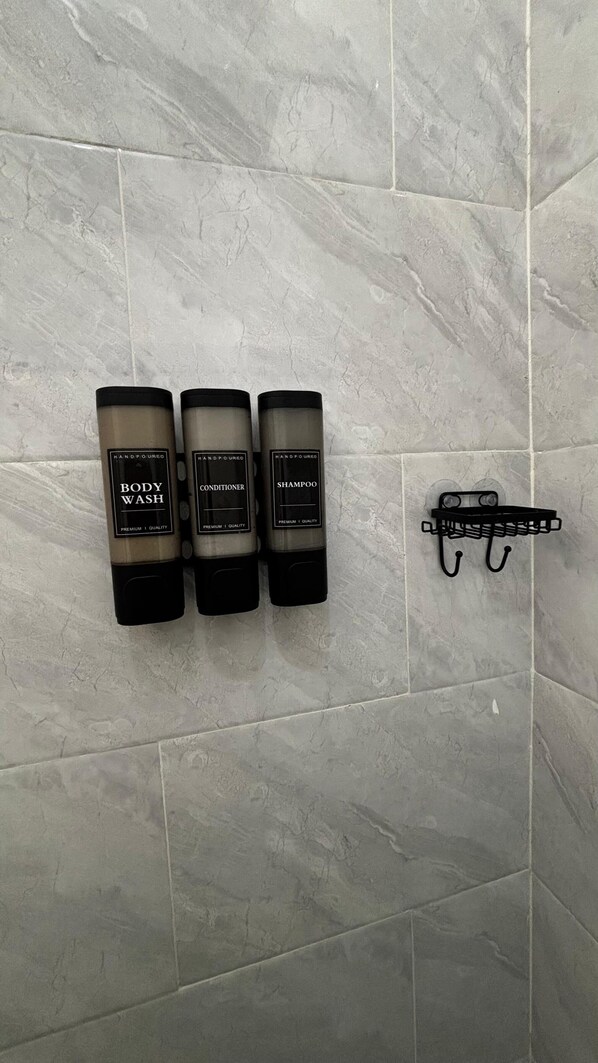 Three toiletry bottles on a wall-mounted rack in a bathroom with grey tiles.