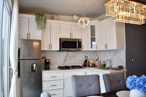 A modern kitchen with white cabinetry, a stainless steel refrigerator, a built-in microwave, and a gas stove. - Coastal Home San Miguel (San Miguel)