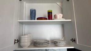 A cabinet with shelves holding stacks of white plates and bowls, a blue vase, and colorful cups.