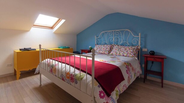 A bedroom with a bed, a yellow dresser, a red nightstand, a blue wall, and a skylight.