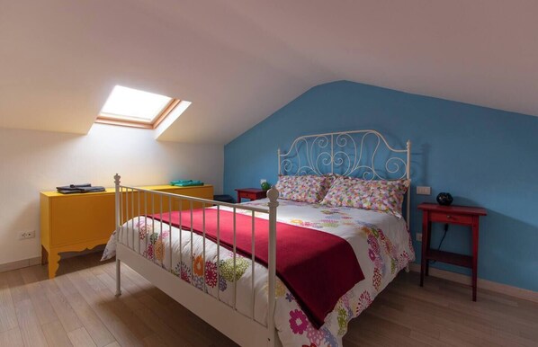 A bedroom with a bed, a yellow dresser, a red nightstand, a blue wall, and a skylight.
