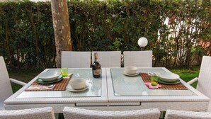 A dining table set with plates, bowls, and a bottle, surrounded by wicker chairs.