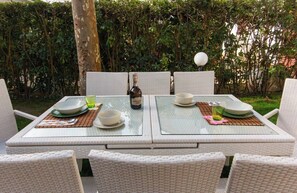 A dining table set with plates, bowls, and a bottle, surrounded by wicker chairs.