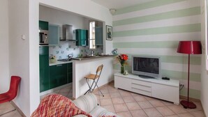 A compact living space with a kitchenette, a television, a red chair, and a striped wall.