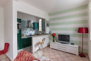 A compact living space with a kitchenette, a television, a red chair, and a striped wall.