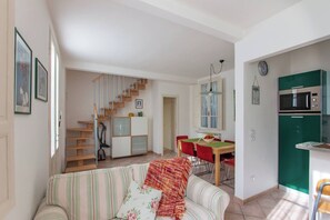 A living room with a sofa, a dining area with a table and chairs, a staircase, and a kitchen with a microwave and refrigerator.