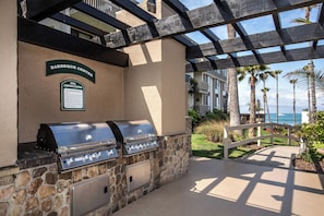 An outdoor barbecue area with a grill and a sign indicating BBQ instructions. - Bahama Hideaway (Oceanside)