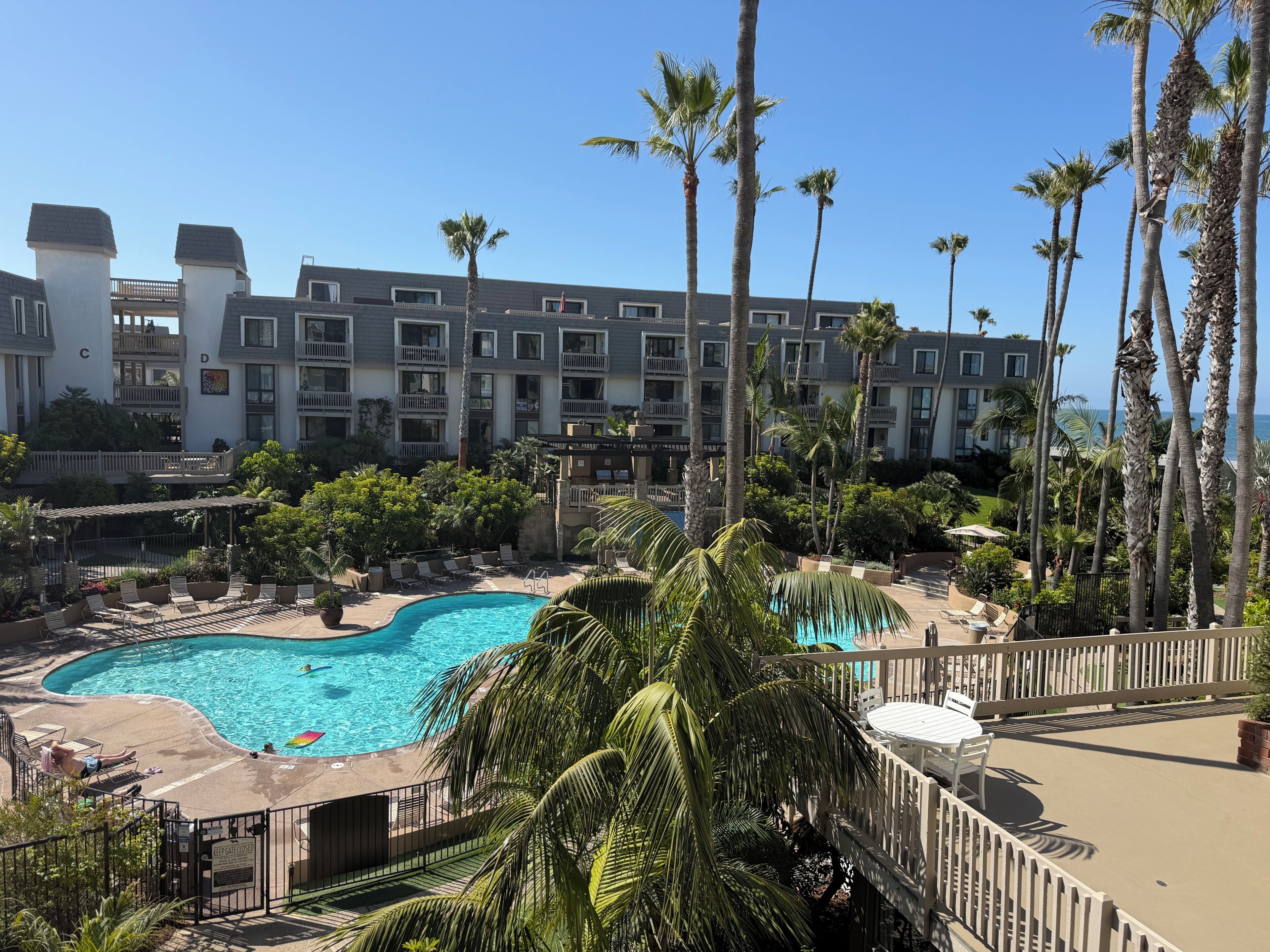 A hotel with a swimming pool, palm trees, and a view of the ocean.