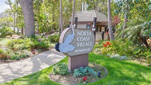 Schild für North Coast Village, 999 North Pacific, umgeben von üppiger Vegetation und einem gepflegten Garten.