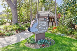 A sign for North Coast Village, 999 North Pacific, surrounded by lush greenery and a well-maintained garden. - One Bedroom Unit With Beautiful Ocean Views From Balcony! (Oceanside)