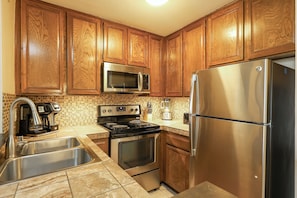 A kitchen with wooden cabinets, stainless steel appliances, a double sink, and a tiled backsplash. - Bahama Hideaway (Oceanside)