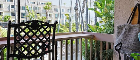 Un balcon avec un parasol rouge, une chaise noire et une poussette.